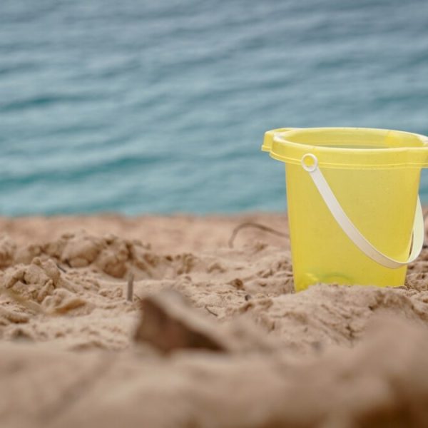 yellow plastic bucket on brown sand near body of water during daytime